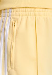 Gele joggingbroeken gemaakt van lichtgewicht stof, met witte zijkstrepen, een elastische tailleband en een zijzak met rits.