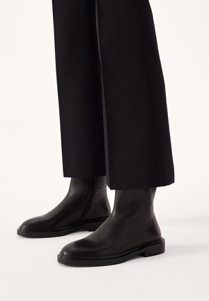 Sorte læder ankelstøvler med en glat overflade, struktureret form, lynlås på siden og en flad gummisål, parret med brede sorte bukser.
