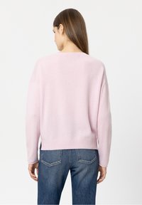 Rosa gestrickter Pullover mit rundem Ausschnitt, überschnittenen Schultern und geripptem Saum. Kombiniert mit blauen Jeans, die eine entspannte Passform zeigen.