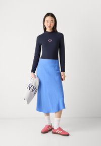 Langermet marinblå topp med logo, blå maxiskjørt, rosa joggesko og grå hettegenser med "GANT" trykket, lagd for en avslappet stil.