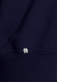 Mörkblått tyg med en strukturerad stickning. Har en vit sydd accent vid fållen. Materialet verkar mjukt och elastiskt.