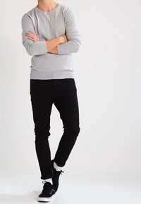 Grijze lange mouwen trui met een ronde hals, gecombineerd met zwarte slim-fit spijkerbroek en zwarte sneakers. De trui heeft geribbelde manchetten en onderzoom.