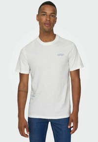 Weißes Baumwoll-T-Shirt mit dem hellblauen NASA-Logo auf der Brust und einem Grafikelement nahe dem Saum. Rundhalsausschnitt und kurze Ärmel.