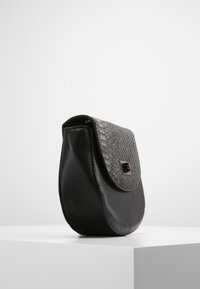 Černá kabelka vyrobená z texturované a hladké kůže, s zakřiveným tvarem, vzorovaným klopou a obdélníkovým detailem sponky.