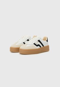 Weißer Sneaker mit schwarzen Streifen, aus Wildleder und Leder, runde Zehenform und tanfarbenem Gummisohle. Verfügt über Schnürsenkel und ein Logo an der Seite.