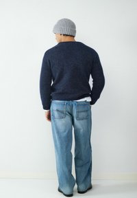 Granatowy sweter z dzianiny, jasnoniebieskie luźne dżinsy i szary, prążkowany beanie; widoczne szwy i kieszenie na dżinsach. Widok z tyłu na białym tle.