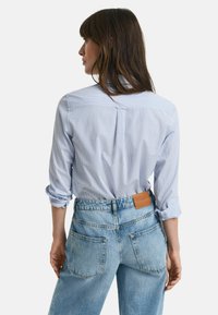 Camicia a righe azzurro chiaro con maniche arrotolate, abbinata a jeans di denim azzurro chiaro a vita alta con etichetta in pelle.