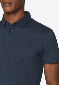 Polo shirt bleu marine avec un tissu texturé, patte de boutonnage et col classique. Manches courtes avec des détails de couture subtils.