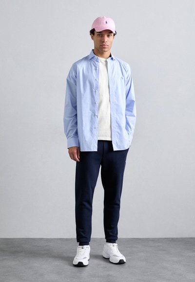 Světle modrá košile na knoflíky přes bílý tričko, navy tepláky a růžová čepice. Bílé tenisky dokončují neformální outfit.