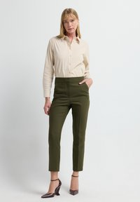 Beige overhemd met knopen, slim-fit groene broek, glanzende donkere hakken en enkelsluiting. Soepele stof met een getailleerde silhouet.