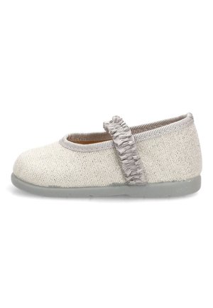 Zapato Mary Jane beige claro para niño, con parte superior de tela texturizada, correa elástica con volantes y suela plana gris, visto de lado.