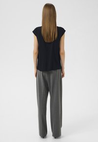 Top nero a maniche corte con taglio dritto, abbinato a pantaloni grigi scivolati con una sottile texture e vita alta.