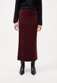 Burgundy gyapjú keverék maxi szoknya egyenes vonalú és puha textúrájú, fekete toppal és fekete hegyes orrú csizmával viselve.