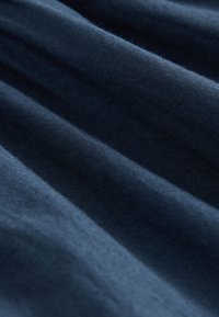 Tela azul marino con una textura suave, que presenta pliegues y sombras sutiles, destacando su color intenso y profundidad.