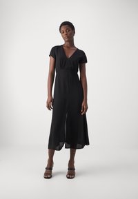 Black, flowy dress with a V-neckline, short sleeves, and mid-length hem. Lightweight fabric with a smooth texture.