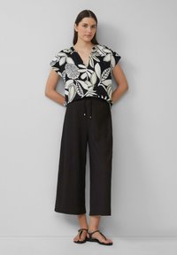 Chemise noire à fleurs à manches courtes avec des motifs de feuilles blanches, assortie à un pantalon noir large et court et des sandales noires à lanières.