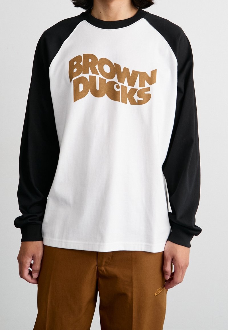 Langärmliges Raglan-Shirt mit schwarzen Ärmeln und weißem Körper. Mit fettem braunem "BROWN DUCKS"-Text auf der Brust. Weicher Baumwollstoff.
