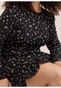 Musta kukkamekko, jossa on tiukka siluetti, pitkät hihat, pieniä ruusukuoseja ja röyhelöhelma lisätekstuuria varten.