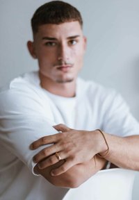 Bracciale e anello in tono dorato su una mano poggiata su un braccio. Il soggetto indossa una t-shirt bianca oversize con le maniche arrotolate, realizzata in un tessuto morbido.