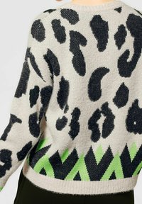 Ljusgrå tröja med svart djurtryck och grönt zick-zack-mönster vid nederkanten. Mjuk textur och avslappnad passform med rundad hals.