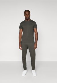 Donkergroene t-shirt met korte mouwen, gecombineerd met bijpassende joggerbroeken, gemaakt van zachte stof. Witte sneakers maken de outfit compleet.