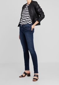 Černá kožená bomber bunda přes pruhované tričko, tmavé džínové skinny jeans a černé sandály na blokovém podpatku s metalickými detaily.