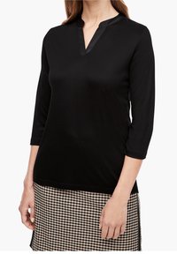 Zwarte, lange mouw top met een hoge kraag en V-hals. Zachte textuur, gecombineerd met een rokje in houndstooth-patroon.