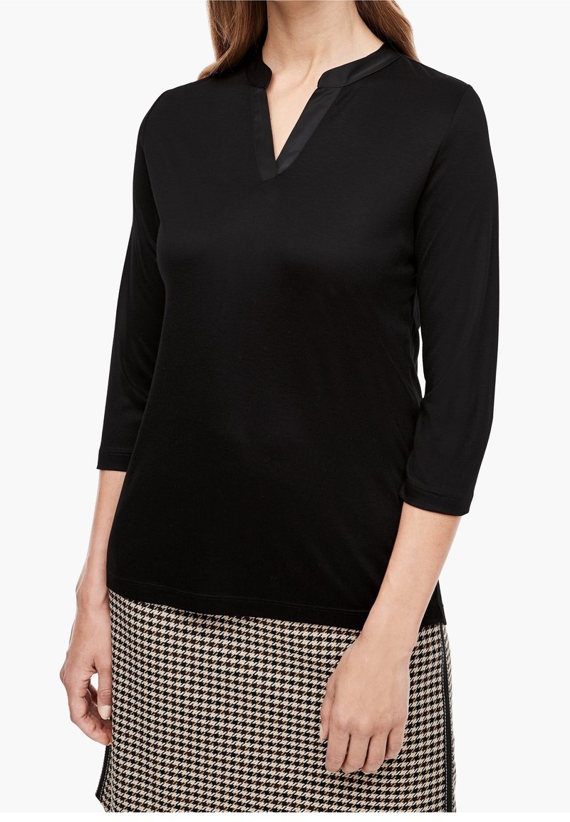 Zwarte, lange mouw top met een hoge kraag en V-hals. Zachte textuur, gecombineerd met een rokje in houndstooth-patroon.