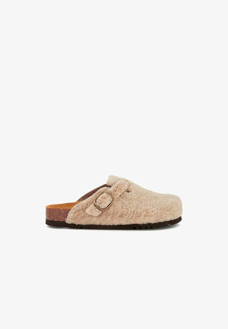 Fuzzy beige slip-on clogs with a buckle detail, cork footbed, and textured outsole for grip. Soft material creates a cozy appearance.