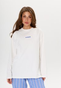 Chemise blanche à manches longues avec un col ras du cou et le texte bleu "MIRONS" sur la poitrine, fabriquée en tissu doux avec une coupe décontractée.