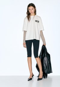 Lys beige oversized t-shirt med trykket "DANCE FIRST THINK LATER". Sorte korte leggings, sorte hæle med nitter og en sort læderjakke.