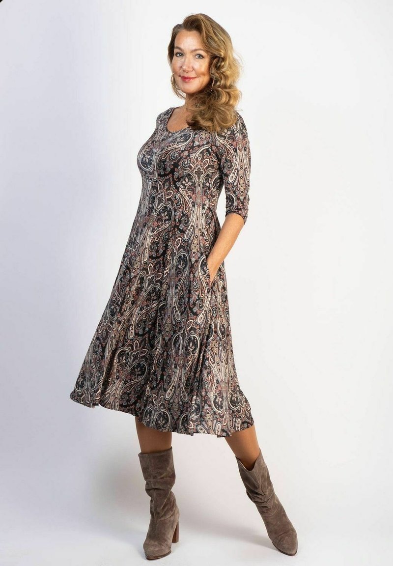 Ein fließendes, knielanges Kleid mit einem Paisley-Muster in dunklen Farben, aus weichem Stoff gefertigt; verfügt über Dreiviertelärmel und seitliche Taschen.