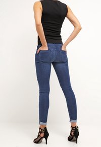 Slanke blå denim jeans med to baglommer, parret med sorte højhælede sandaler. Jeansene har en glat tekstur og en tætsiddende pasform.