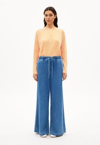 Gestreepte lange mouwen top in oranje en geel; gecombineerd met brede spijkerbroek in blauw met een elastische tailleband en trekkoord.