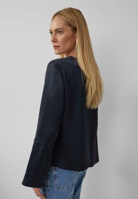 Marineblauw langemouwtop met een zachte textuur en uitlopende mouwen, gecombineerd met lichte denim jeans met decoratieve studs op de zak.