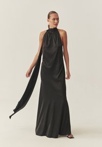 Vestido de raso negro con cuello halter y un detalle de capa drapeada, que presenta un cuello alto y una silueta fluida que se estrecha en el dobladillo.