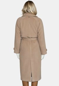 Beżowy wełniany płaszcz z paskiem w talii, usztywnionym kołnierzem i bocznymi rozcięciami, charakteryzujący się gładką teksturą i subtelnymi detalami szwów.