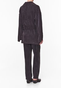 Conjunto de ante en gris oscuro que incluye una chaqueta con cinturón y pantalones a juego. La chaqueta tiene un corte holgado y hombros caídos, con bolsillos laterales.