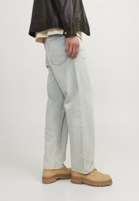 Ljust blå, slitna denimjeans med rak passform, kombinerat med tanfärgade snörkängor och en svart läderjacka.