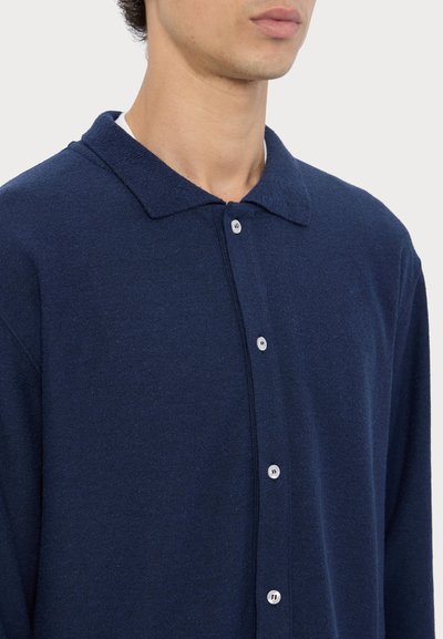 Polo a maniche lunghe di colore blu navy, realizzato in tessuto texture, con chiusura a bottone e un design classico del colletto.