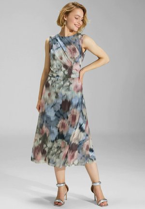 Kwiatowa sukienka midi z bezrękawnym fasonem, warstwową teksturą w pastelowych kolorach: niebieskim, różowym i zielonym, zestawiona z srebrnymi sandałami na obcasie.