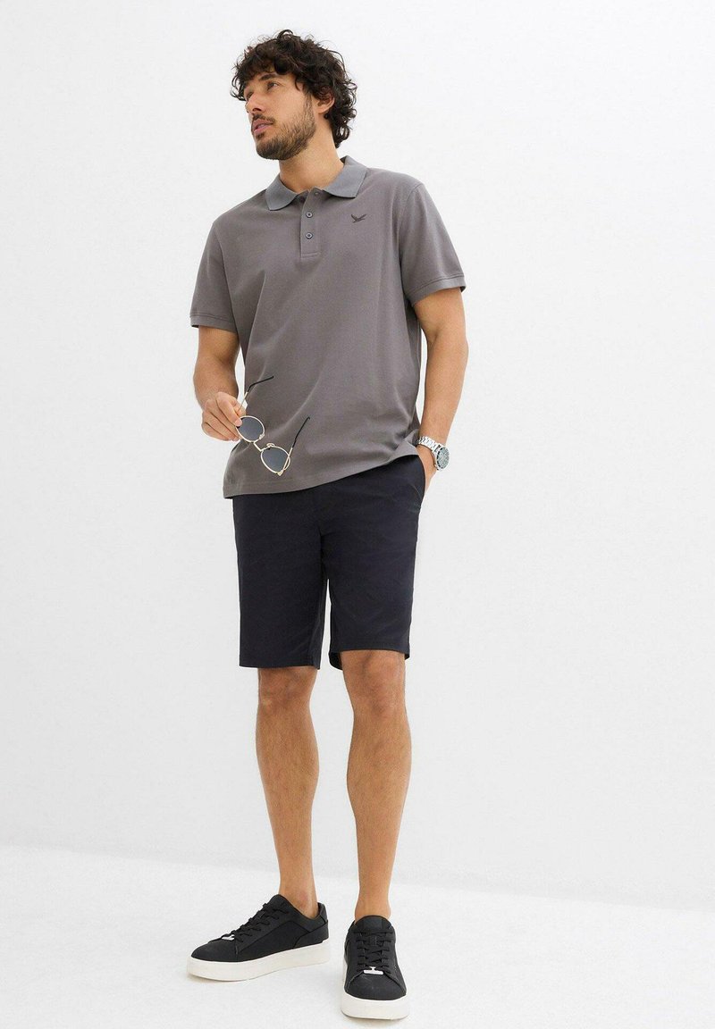 Polo grigio con colletto e logo, abbinato a pantaloni corti scuri. Sneakers nere completano il look. Stile casual, design semplice.