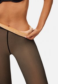 Medias negras transparentes con un patrón texturizado, que cuentan con una cinturilla suave beige en contraste, estando bajadas a la altura de la cadera.