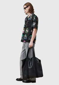 Bolso tote de cuero negro con dos asas resistentes, cierre de cremallera y correas de tela en contraste, que presenta una textura suave y un diseño minimalista.