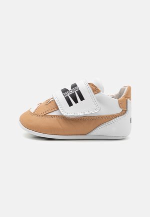 Chaussure pour bébé Moschino beige et blanche, avec une large bride blanche à fermeture auto-agrippante et un logo noir, vue de profil sur un fond uni.