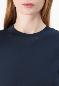 Tmavě modrá mikina s ribovaným výstřihem ve tvaru lodi, hladkou texturou a přiléhavým střihem, která prezentuje jednoduchý a čistý design.