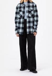 Rutig skjorta i flanellstyg i ljusblått och svart, med två bröstfickor, knappstängning och långa ärmar, i kombination med svarta byxor.