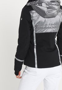 Schwarze Jacke mit grauen Nylonakzenten, ausgestattet mit Kapuze und reflektierenden Streifen. Hergestellt aus einer Mischung weicher Materialien, hat sie eine taillierte Silhouette.