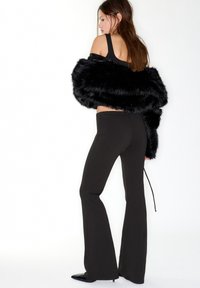 Schwarzer Kunstpelz-Schal über einem schwarzen Tanktop und eng anliegenden, schwarz ausgestellten Hosen mit Reißverschluss am Knöchel, die eine schlanke Silhouette betonen.