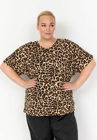 Blůza s krátkým rukávem v leopardím vzoru v béžových a hnědých tónech, má volný střih a výstřih do V. Hladká látka s jemnou texturou.